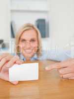 Blonde smiling businesswoman pointing at a card crouching behind