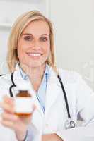 Smiling blonde doctor holding medicine to camera