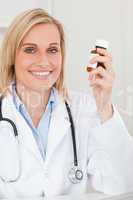 Smiling blonde doctor holding medicine looks into camera