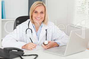 Doctor writing something down holding medicine looks into camera