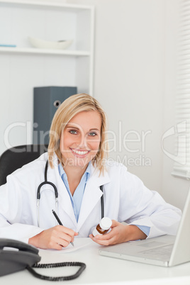 Doctor writing something down while holding medicine looks into