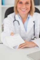 Smiling blonde doctor giving prescription looks into camera