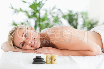 Smiling blonde woman lying on a lounger with stones and candles