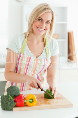 Gorgeous woman cutting green pepper looks into camera