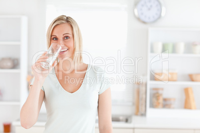 Charming woman drinking water while standing looks into camera