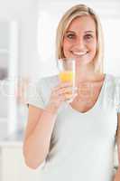 Charming woman holding glass filled with orange juice looking at