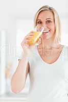 Cute woman drinking orange juice looking into the camera