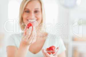 Close up of a young woman enjoying eating strawberries looking i