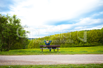 male resting on the bench on the field of dandelions