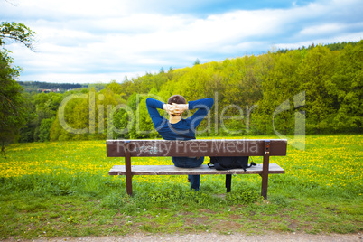 male resting on the bench on the field of dandelions