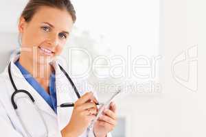 Close up of a smiling brunette doctor writing something down loo
