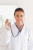 smiling brunette doctor presenting a stethoscope looking into th