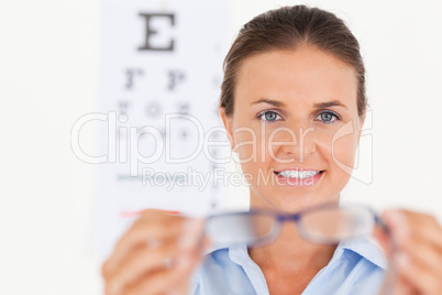 Portrait of a brunette eye specialist handing out glasses lookin