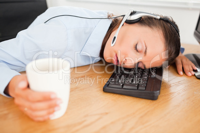 Businesswoman with headset sleeping in office with coffee