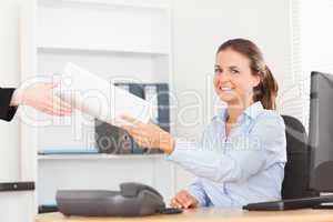 smiling businesswoman receiving a pile of paper looking into the