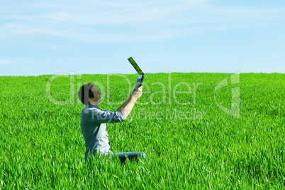 young man uses a laptop in the green field