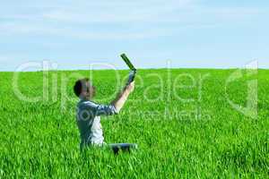 young man uses a laptop in the green field