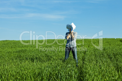 young man covering the face paper in green field