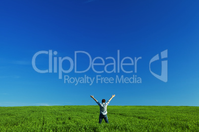young man outstretched arms in green field against the blue sky