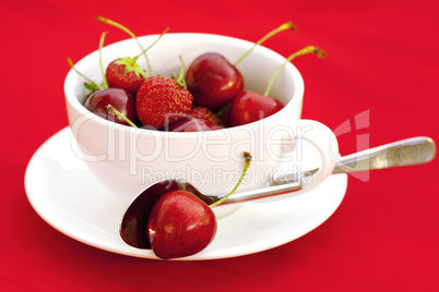 cup saucer spoon cherry and strawberry on a red background
