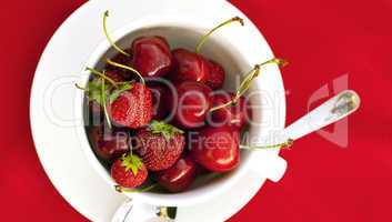 cup saucer spoon cherry and strawberry on a red background