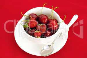cup saucer spoon cherry and strawberry on a red background