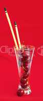 glass with cherries and  with chopsticks on a red background