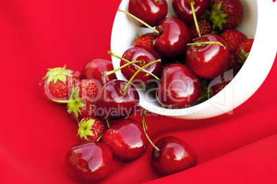 cherries and strawberries in a white cup on a red background