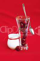 milk jug with a ribbon  glass of cherry and spoon on a red backg