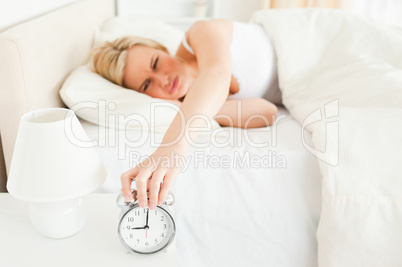 Tired woman switching off her alarm clock