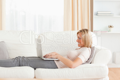 Woman using a laptop while lying on a sofa