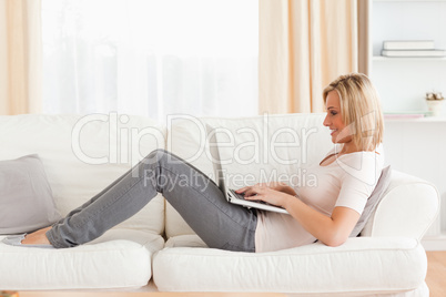 Cute woman using a laptop while lying on a sofa