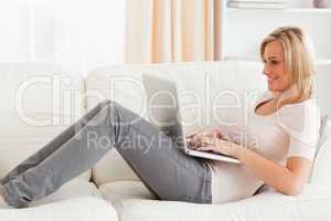Smiling woman using a laptop while lying on a sofa