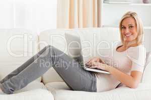 Smiling woman with a laptop while lying on a sofa