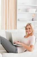 Portrait of a cute woman lying on a sofa with a laptop