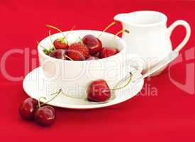 milk jug cup saucer spoon cherry and strawberry on a red backgro