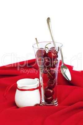 milk jug with a ribbon  glass of cherry and spoon on a red backg