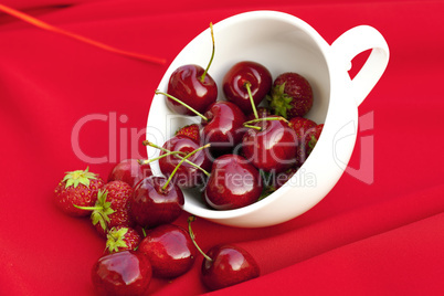 cherries and strawberries in a white cup on a red background