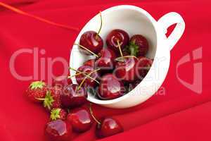 cherries and strawberries in a white cup on a red background