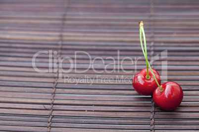 two cherries in plate on a bamboo mat