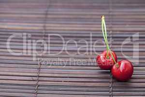 two cherries in plate on a bamboo mat