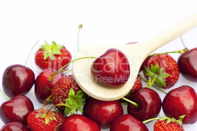 cherry and strawberry in a wooden spoon isolated on white