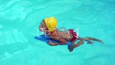 Little girl in yellow swimming hat floats at pool.