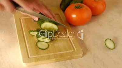 Young woman on kitchen table knifes cucumber.