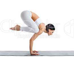 Young woman in white doing yoga pose arm balance