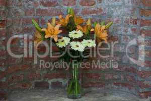 flowers in a vase standing in the background of a brick wall