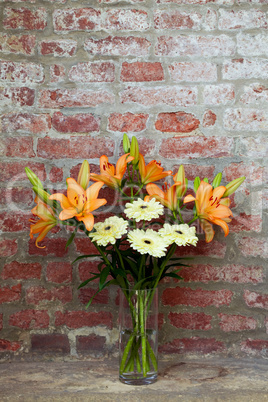 flowers in a vase standing in the background of a brick wall