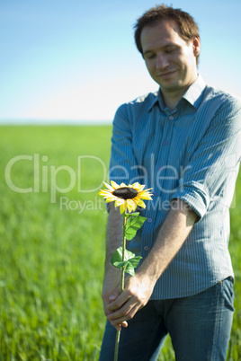 young man standing with a sunflower in the green field