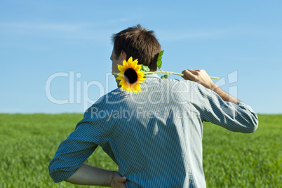 young man standing with a sunflower in the green field