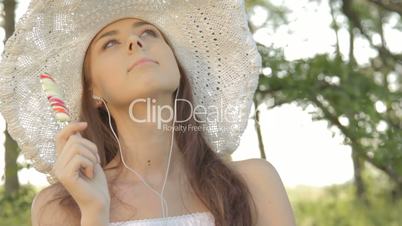Young woman listening music and licking candy, rest on nature in forest